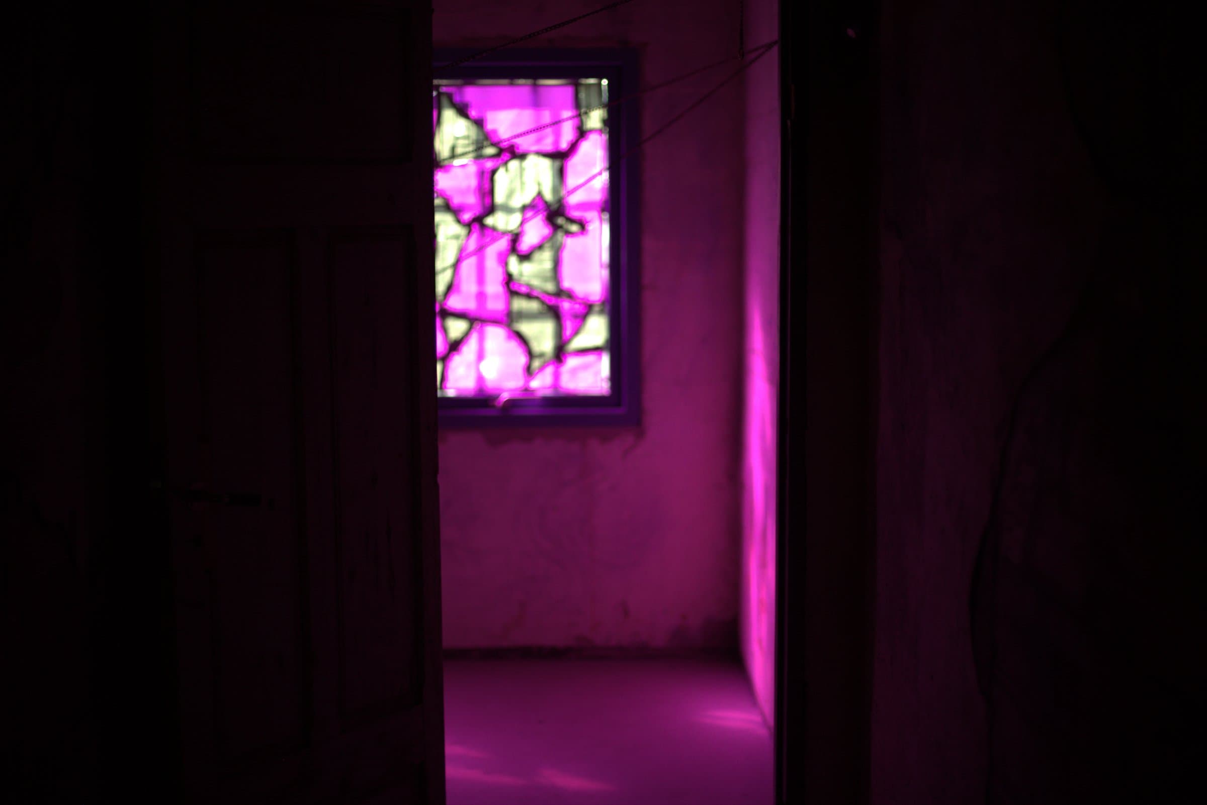 View through a doorway down a corridor toward the glowing magenta stained-glass window