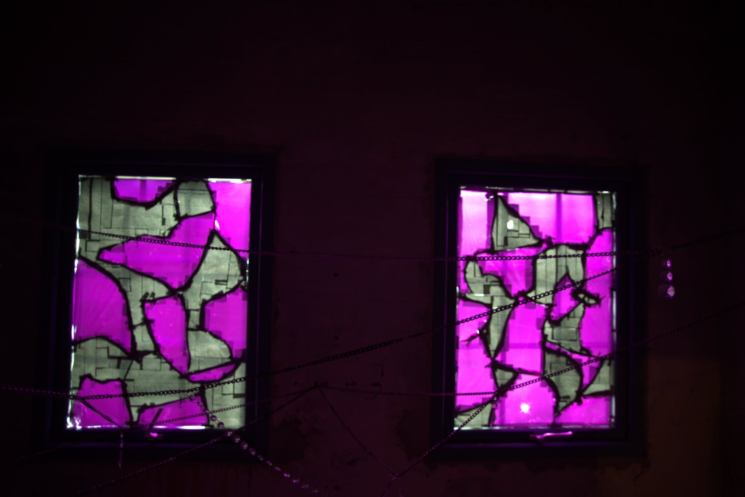 Two magenta stained-glass windows side by side, beaded chains strung across the room in front of them