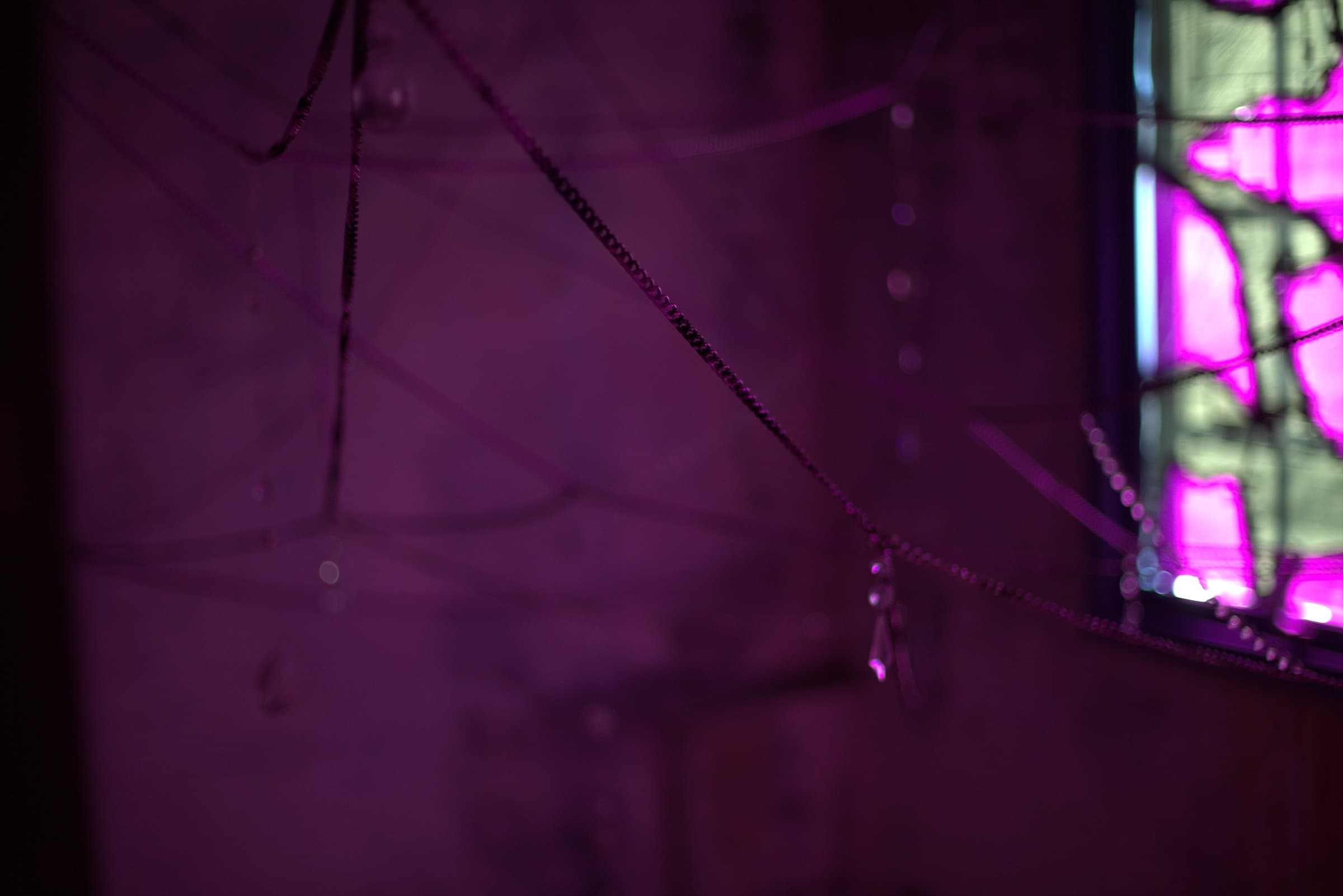 Close-up of beaded chains crossing in the foreground, the magenta window blurred in the background
