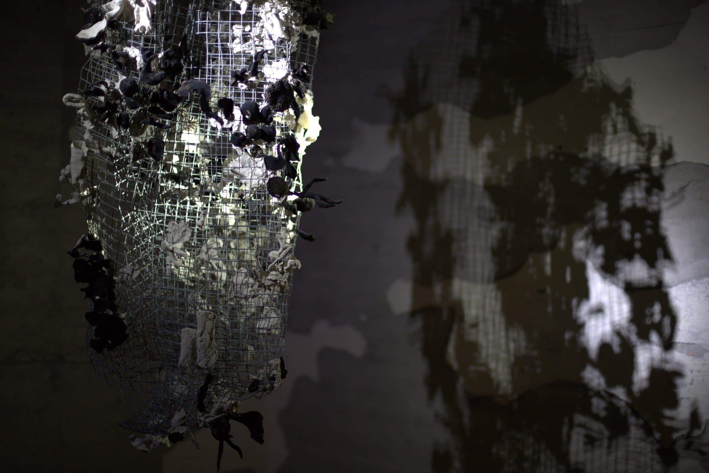 Detail of the hanging sculpture, ceramic pieces set into wire mesh against the concrete wall
