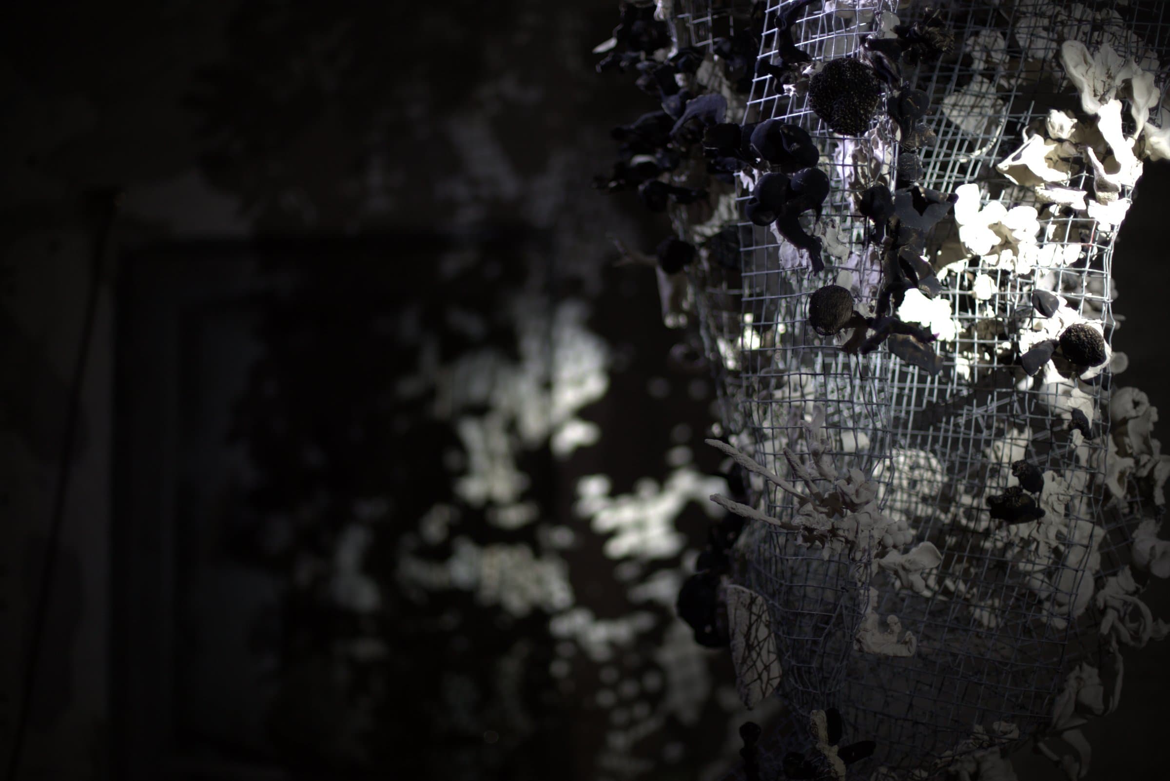 Close-up detail of dark and white ceramic pieces set into the wire mesh form