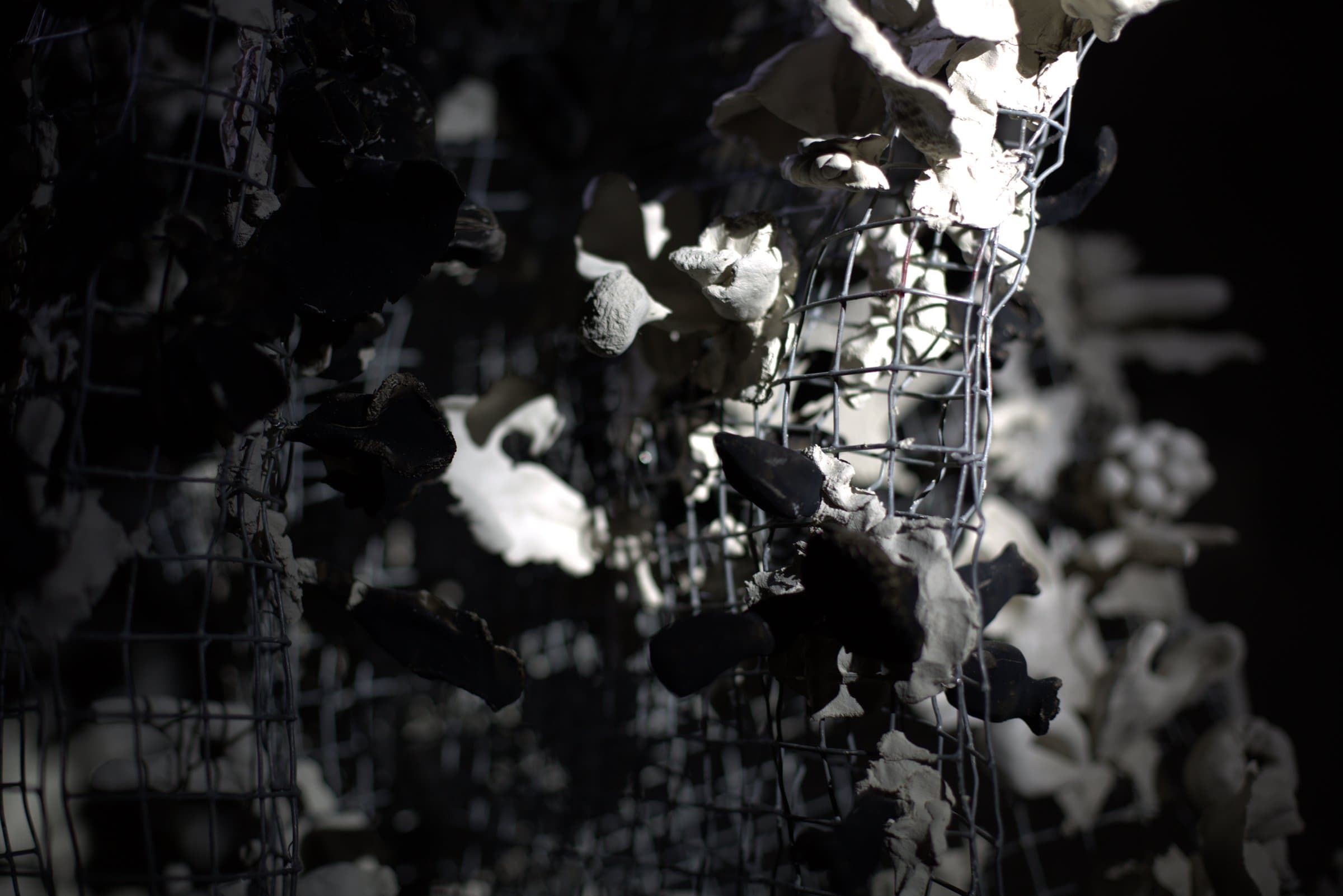 Close-up detail of the sculpture from below, ceramic pieces catching light against the dark interior
