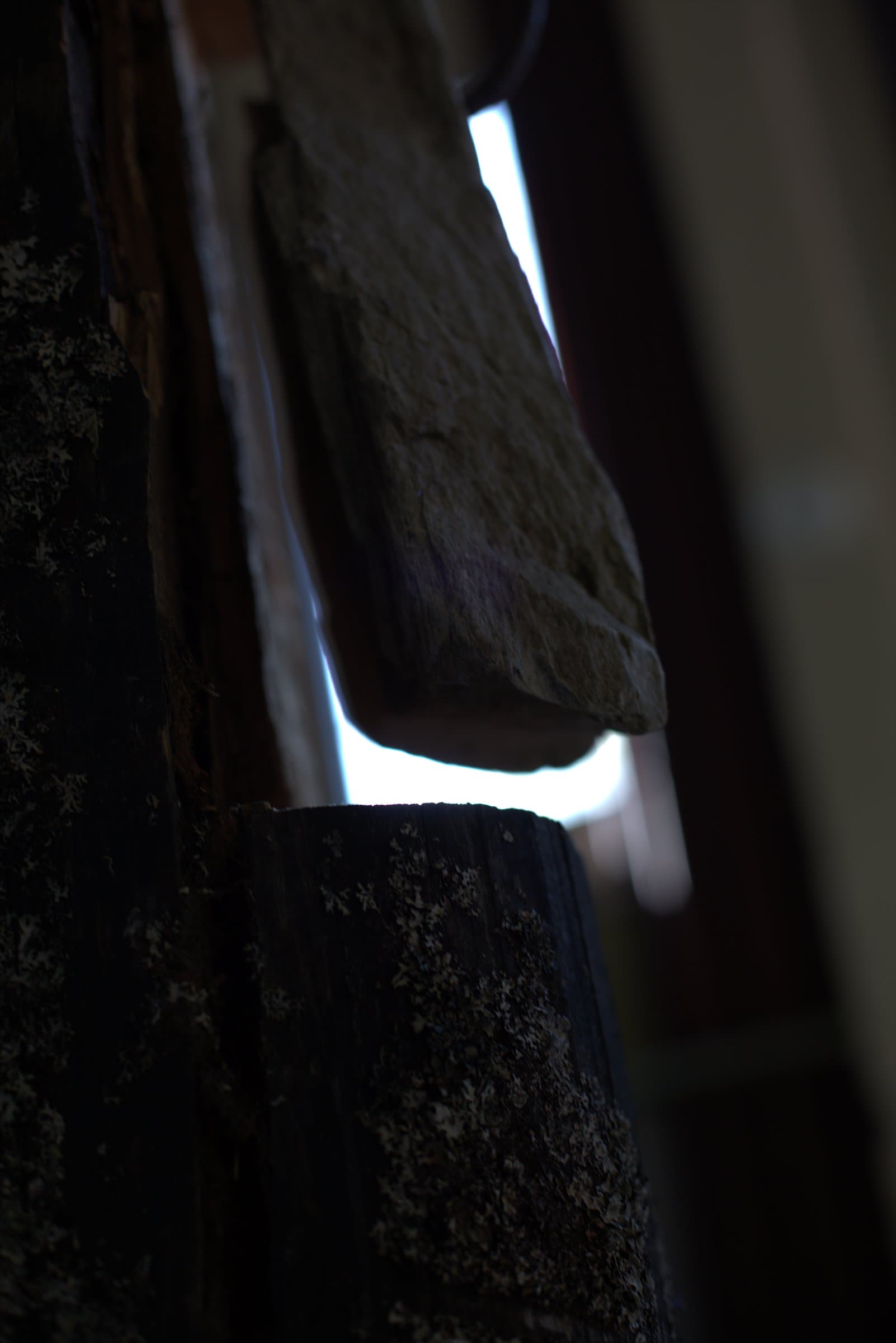 Close-up of a stone resting against a leaning wooden plank, backlit by a doorway