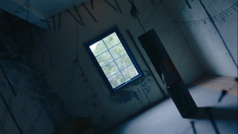 The leaning wooden plank and stone sculpture seen through a window, daylight coming through