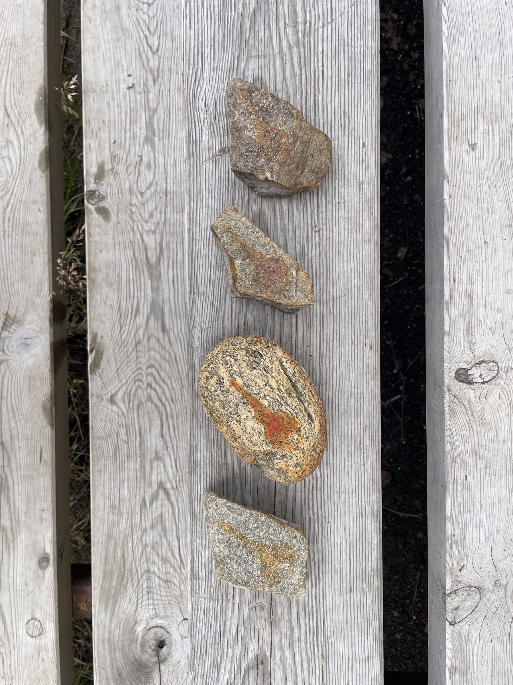 Four stones laid in a row on weathered wooden planks, each marked with a rust-orange key shape