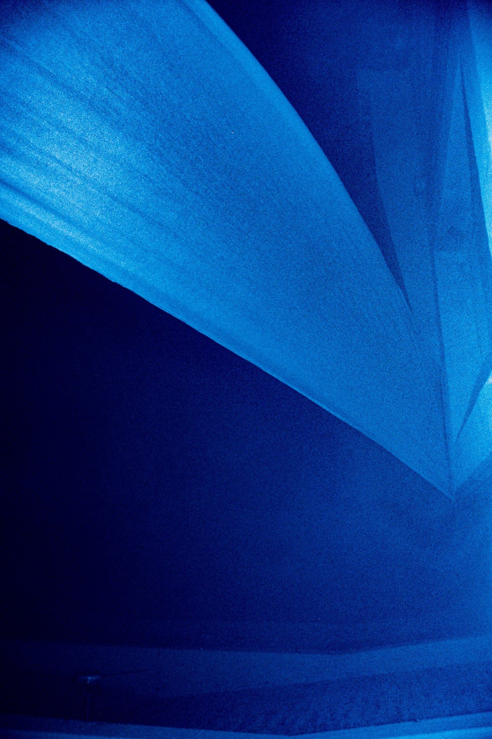 Looking up at blue-lit draped fabric sails meeting at a sharp angle in a dark corner