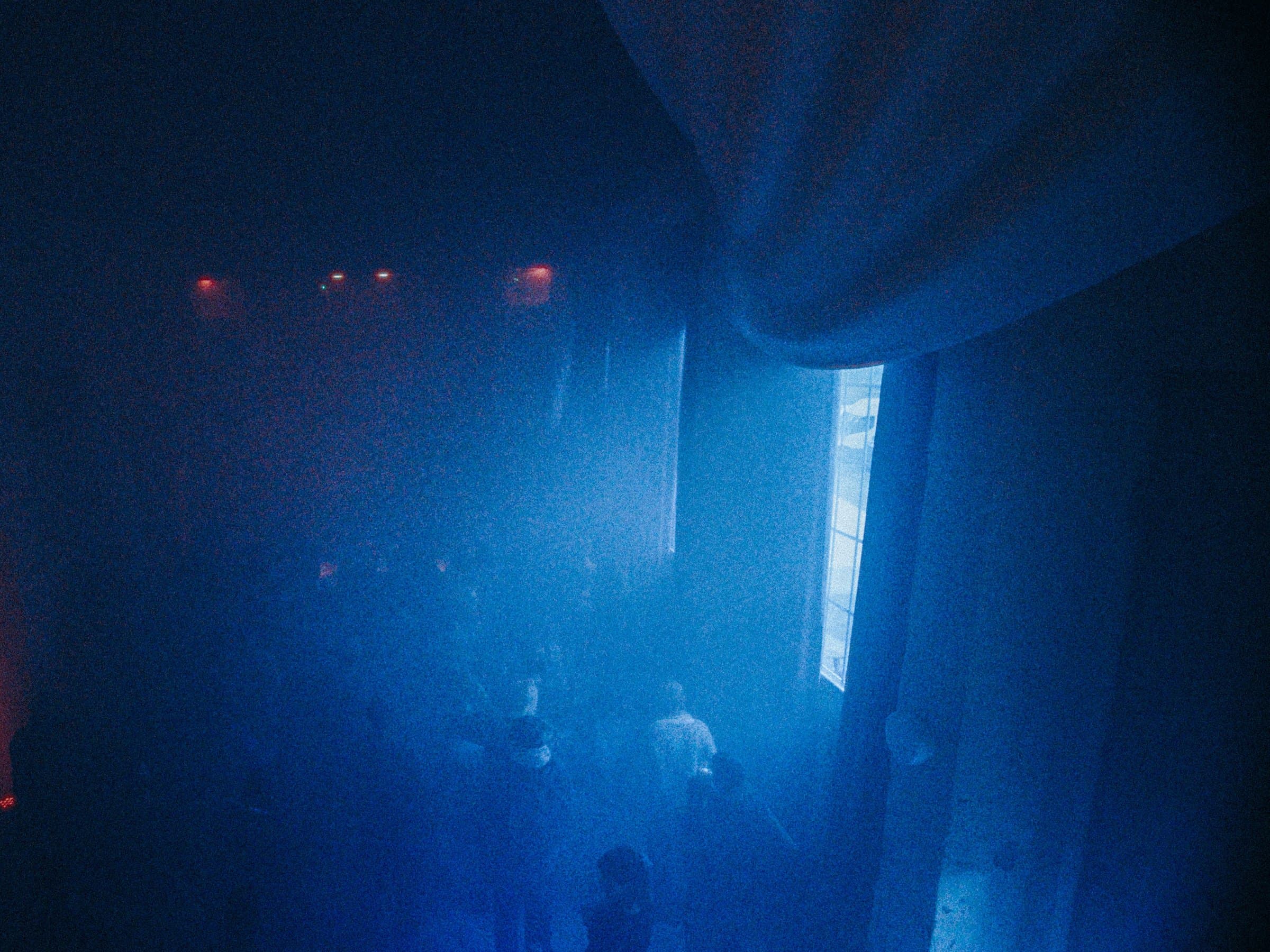A pale blue room with a curved ceiling and a lit window, silhouettes of people gathered on the floor below