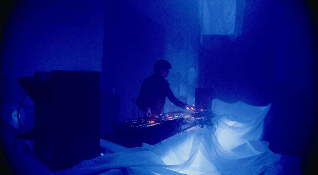 A DJ booth lit blue, draped white fabric beside the decks