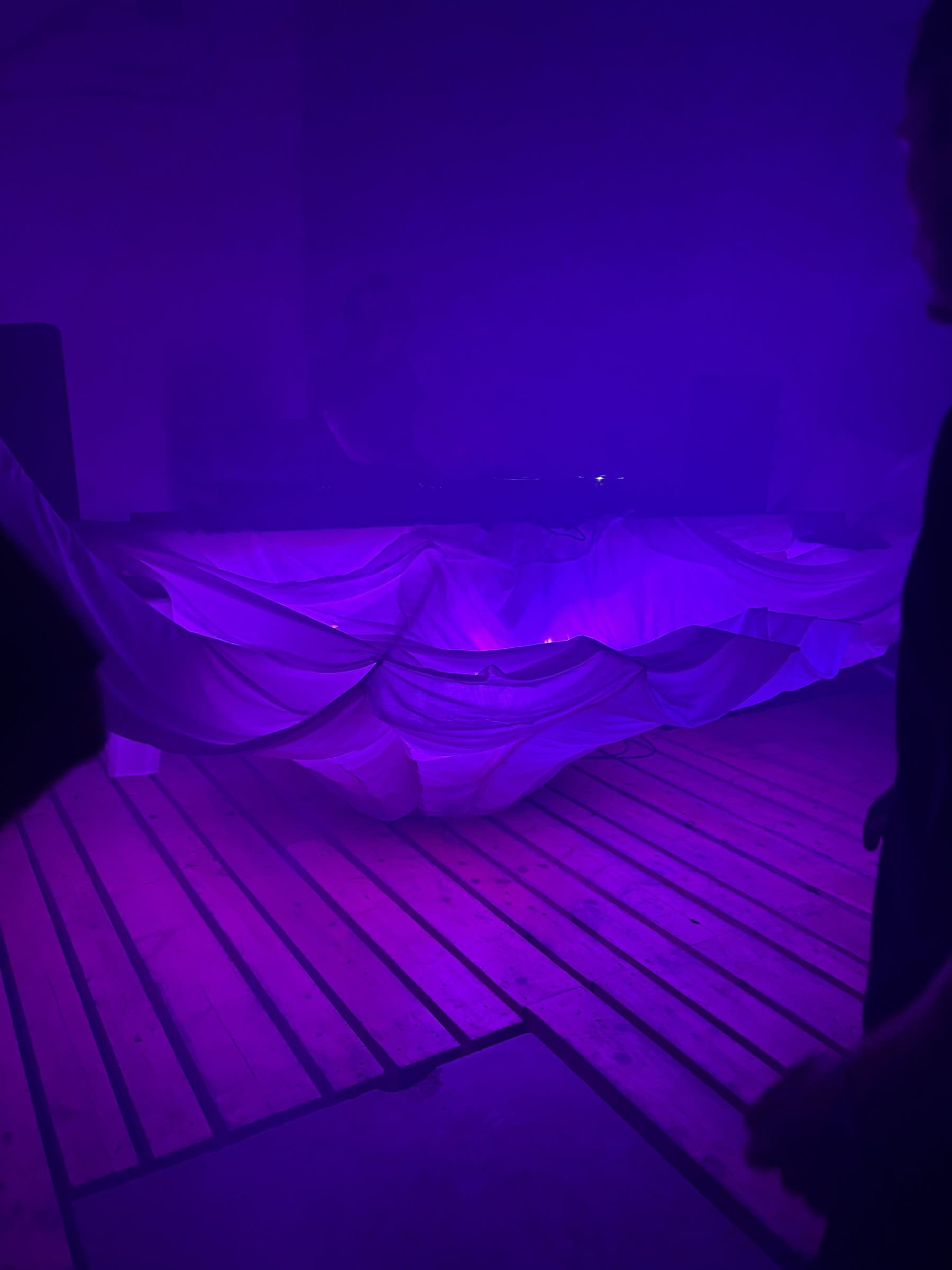 A purple-lit draped white fabric structure on the floor, seen from a different angle