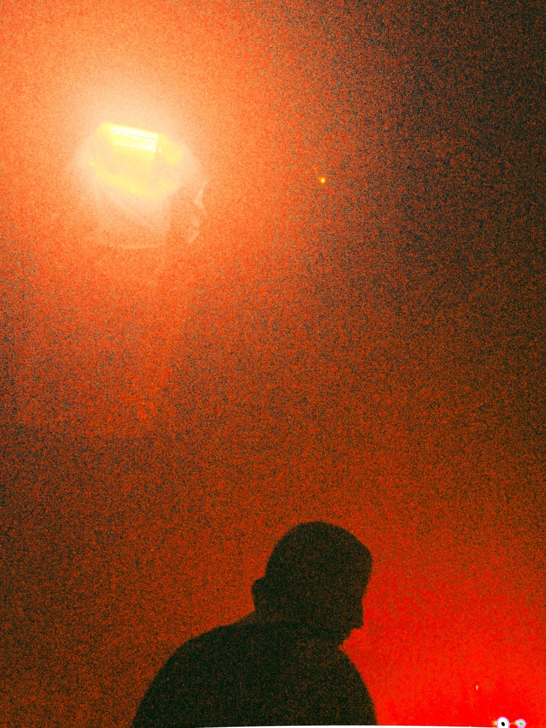A person silhouetted beneath a bright stage light in a red-lit haze