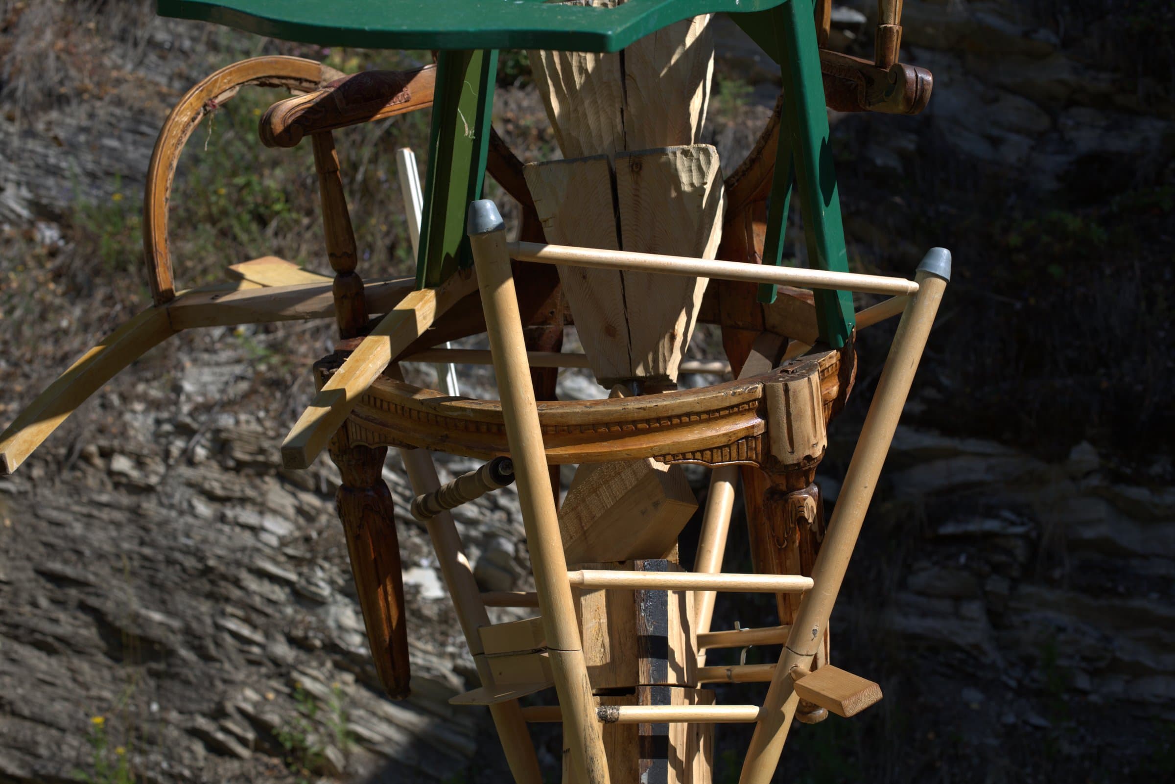 Close-up of the upper part of the sculpture, showing the green painted chair and carved wooden chair legs stacked together