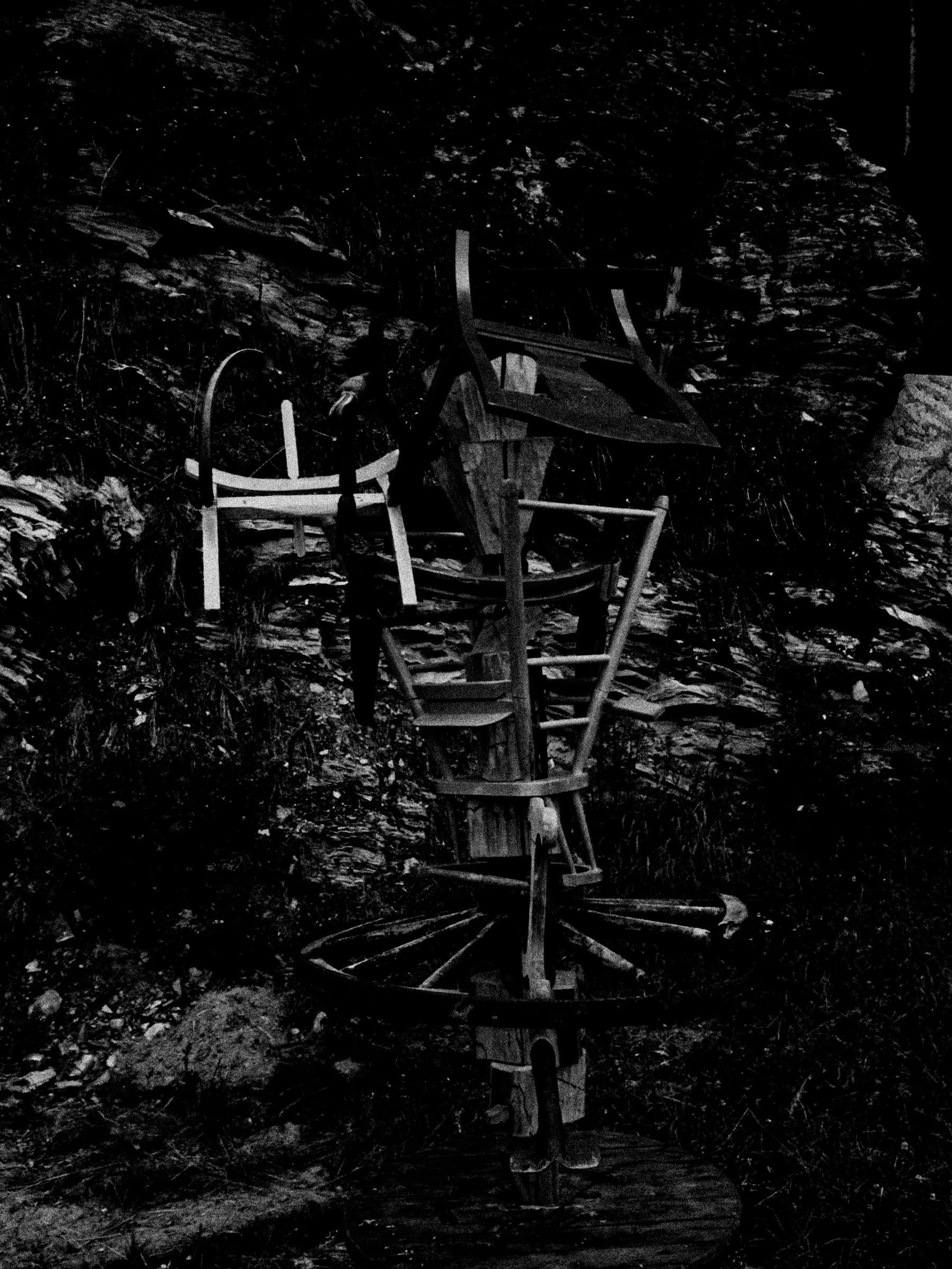 Night flash shot of the sculpture against the dark cliff face, the pale chair and wheel spokes standing out against the black background