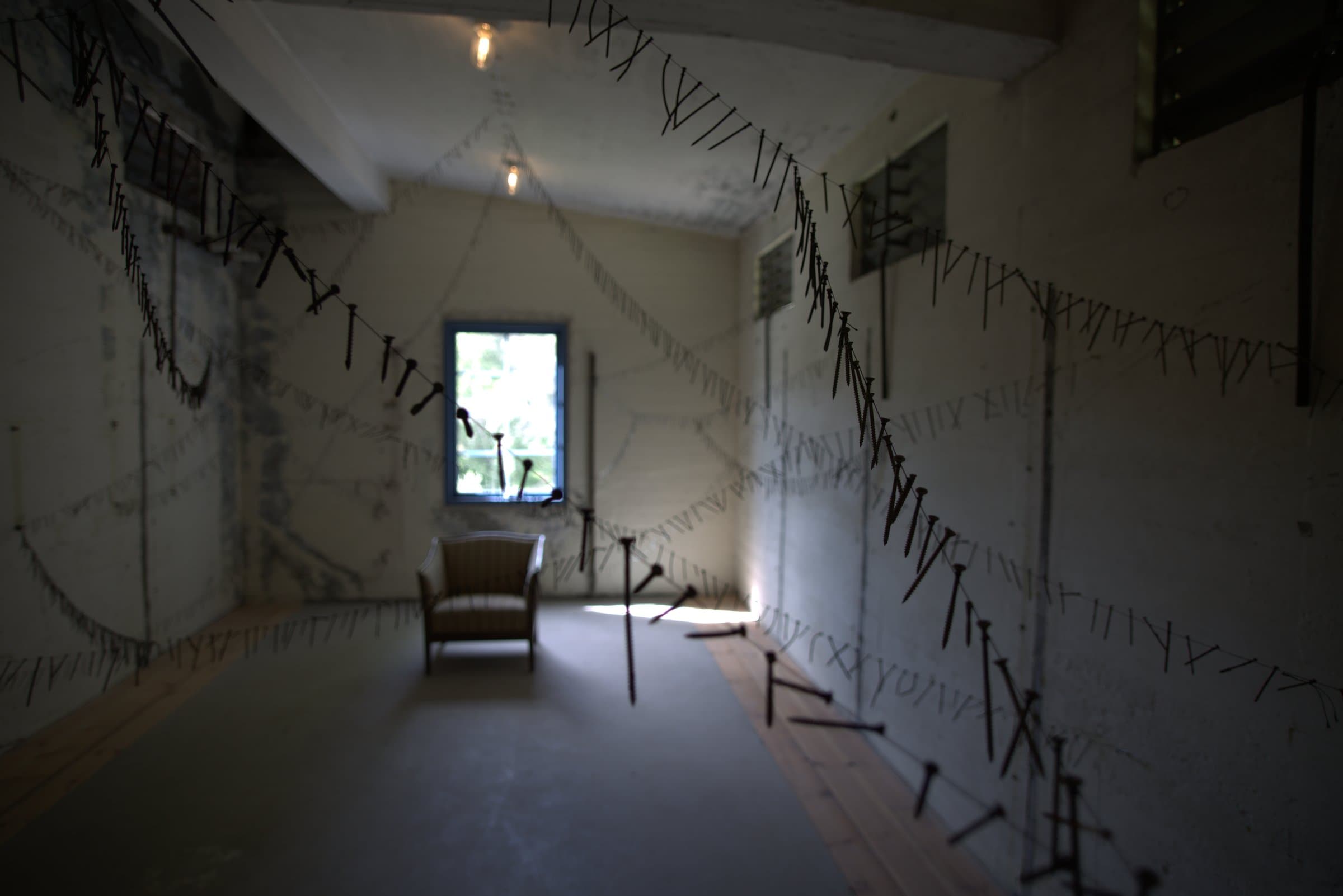 The same room seen from another angle, wires of hanging nails crossing overhead and along the walls, loose nails scattered near the floor