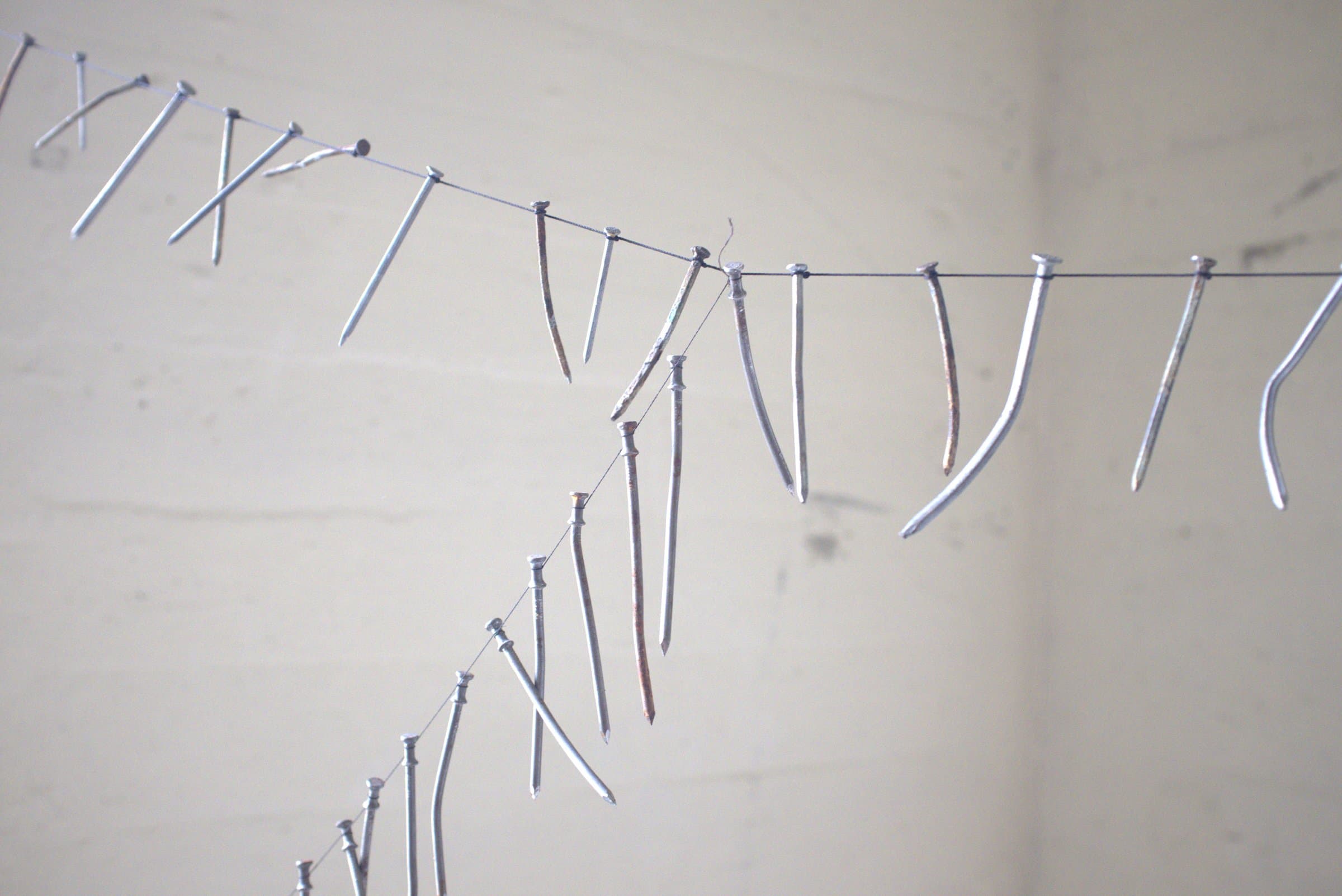 Close-up of several wires strung with bent nails and screws against a bare concrete wall
