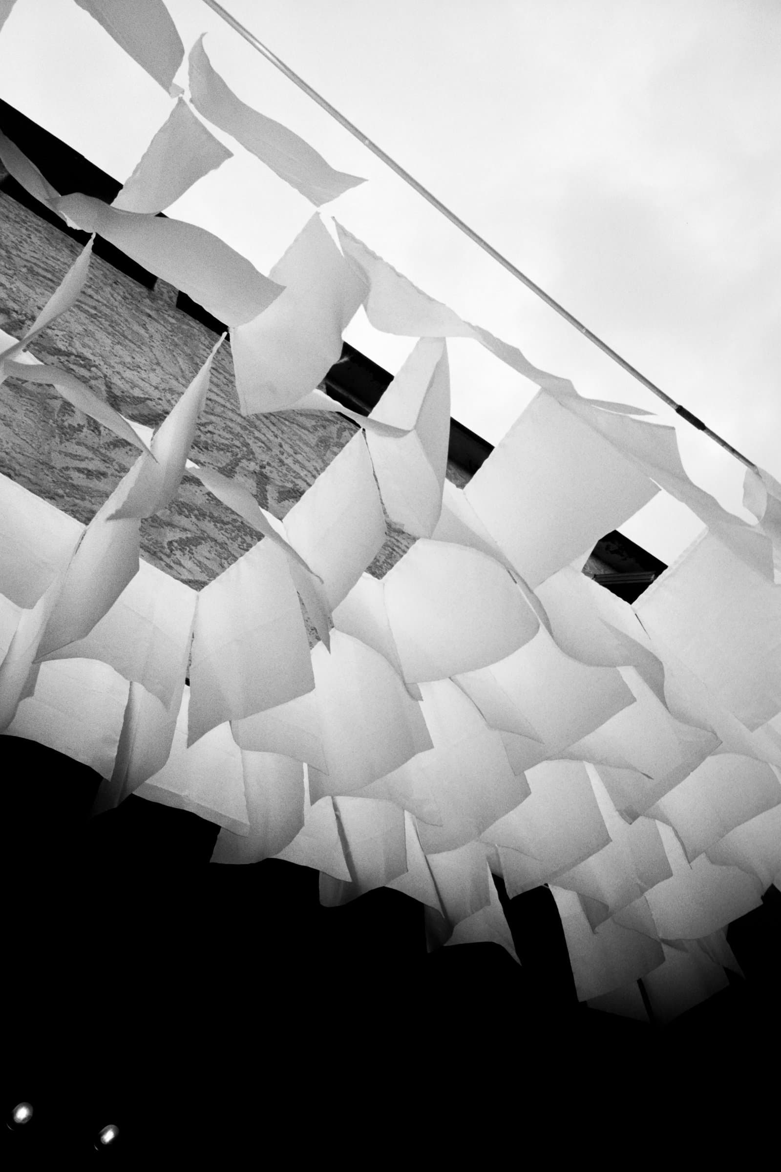 Black and white view looking straight up at the fabric flags hanging beneath the roof edge, a window visible behind them