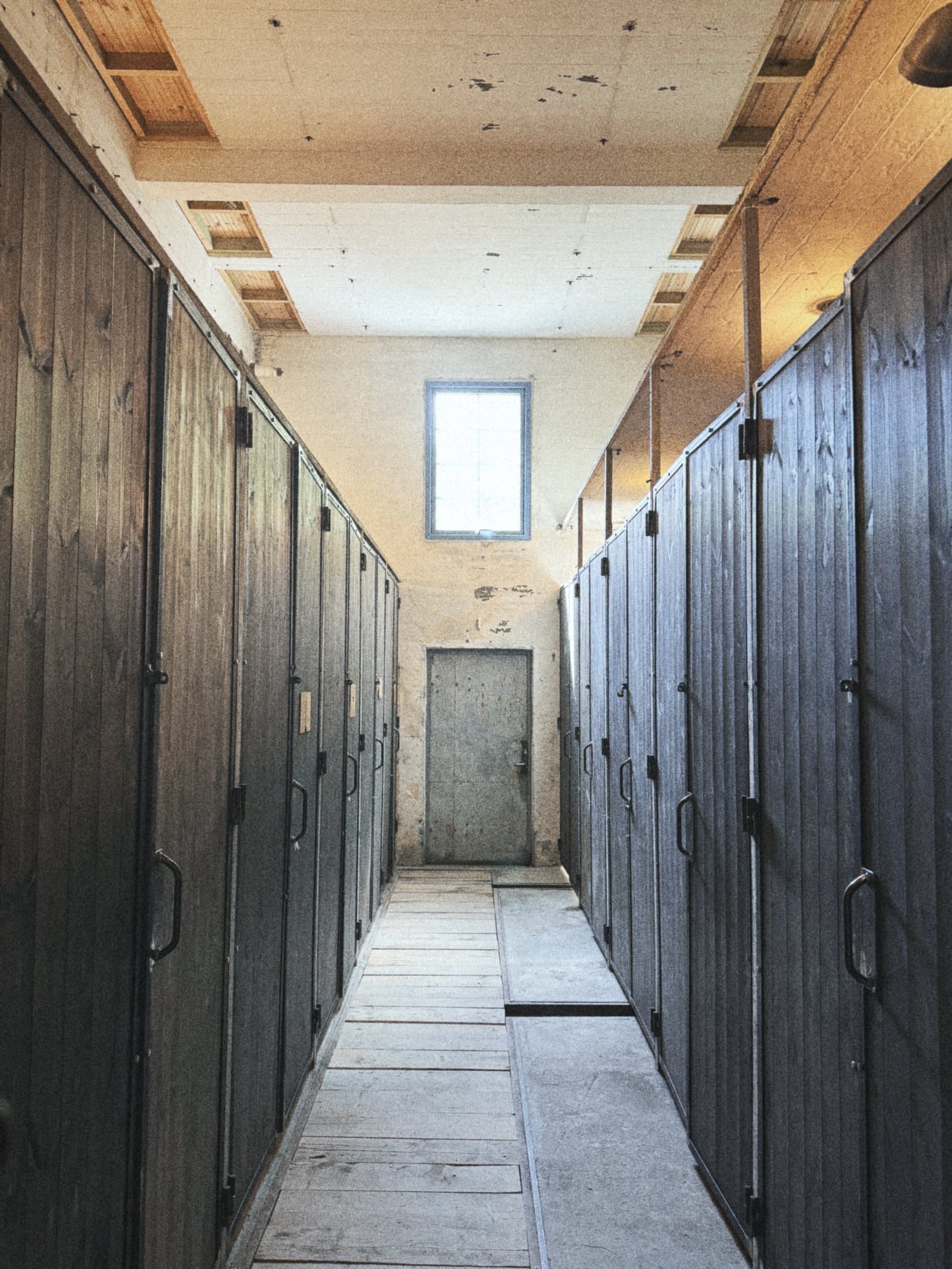 A long corridor lined with tall dark wooden doors to the toilets and showers, a window at the far end.