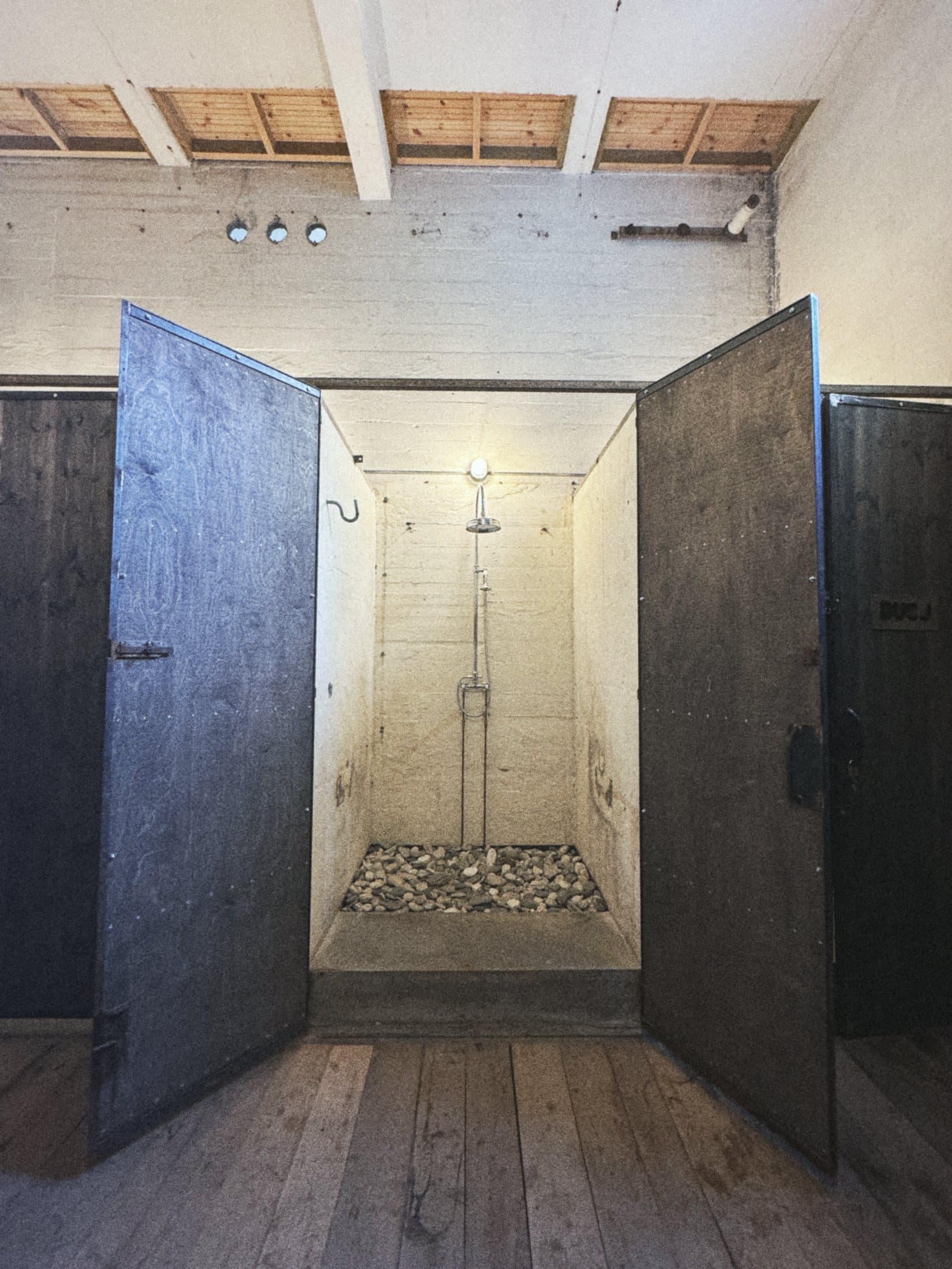Two dark wooden doors open on a shower with a pebble floor.