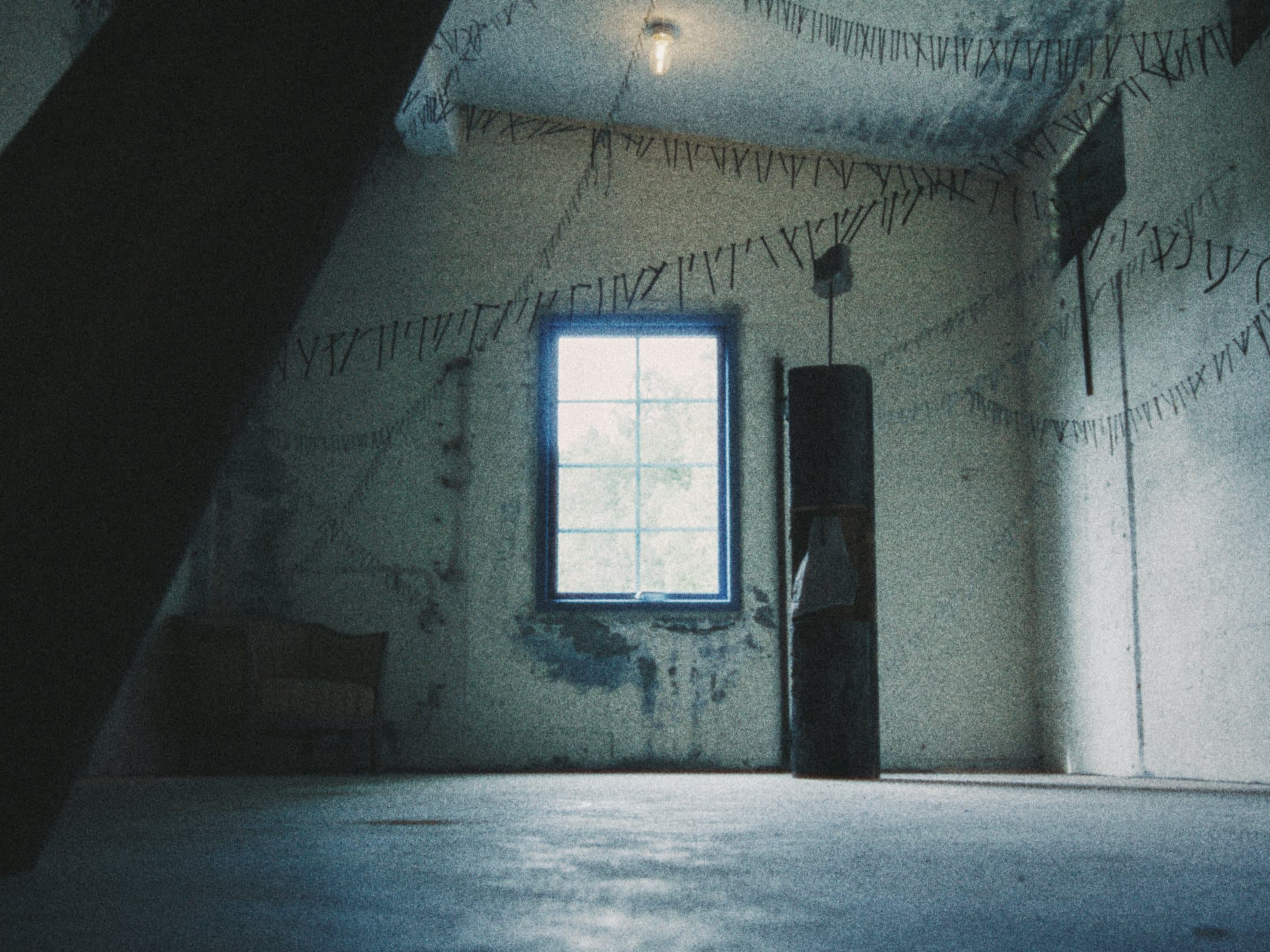 An empty concrete room in blue light, a single window and bunting along the wall.