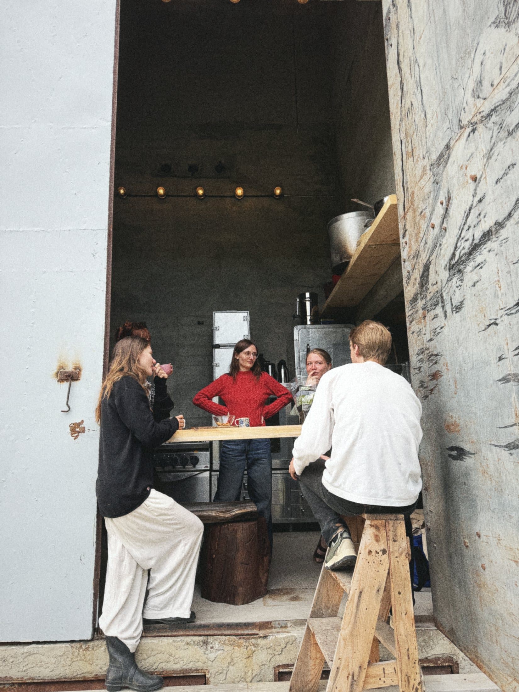 The kitchen seen through its wide open steel doors, people standing and sitting at the counter inside.