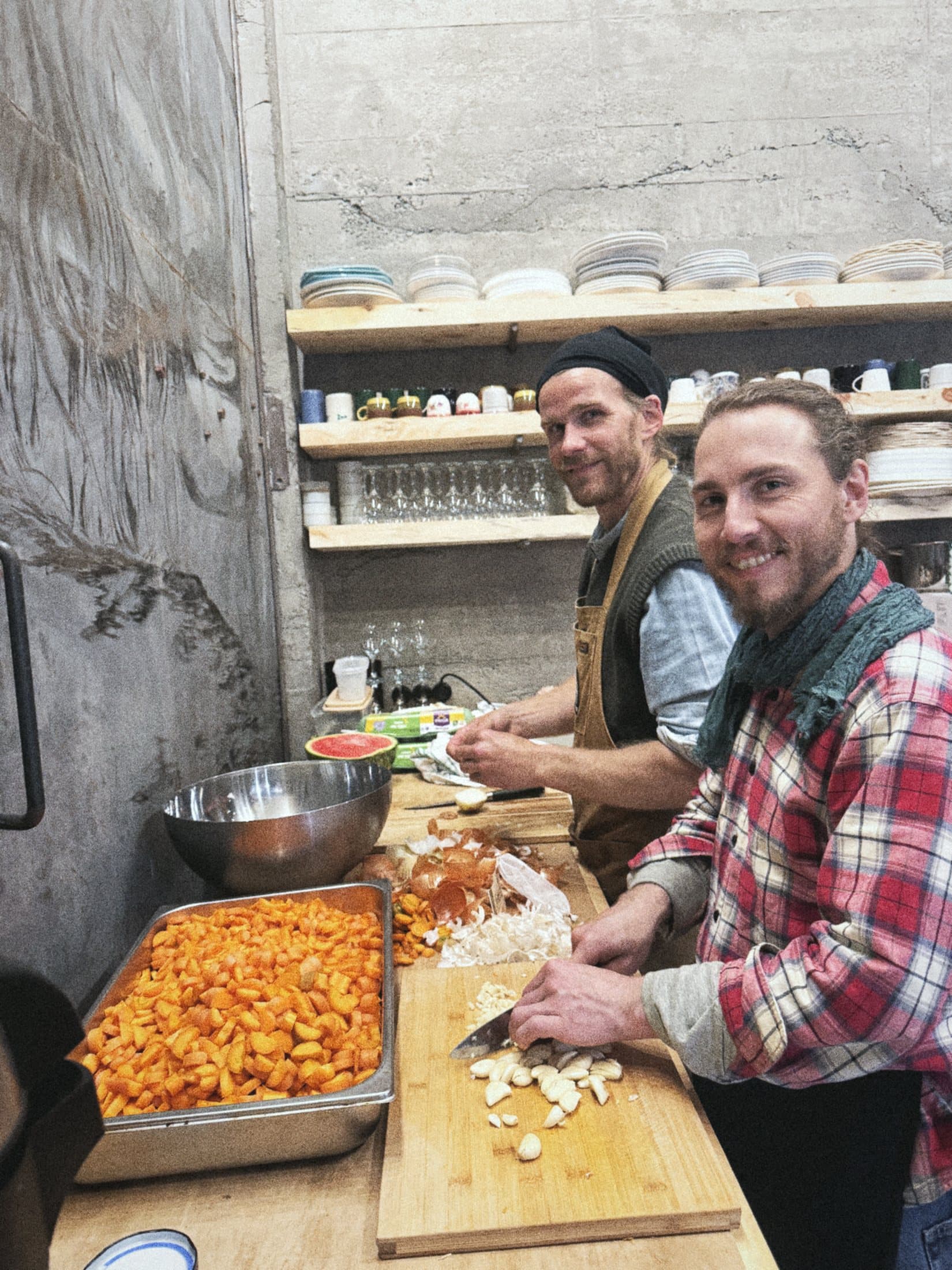 Two people chopping vegetables at the kitchen counter, shelves of plates behind them.