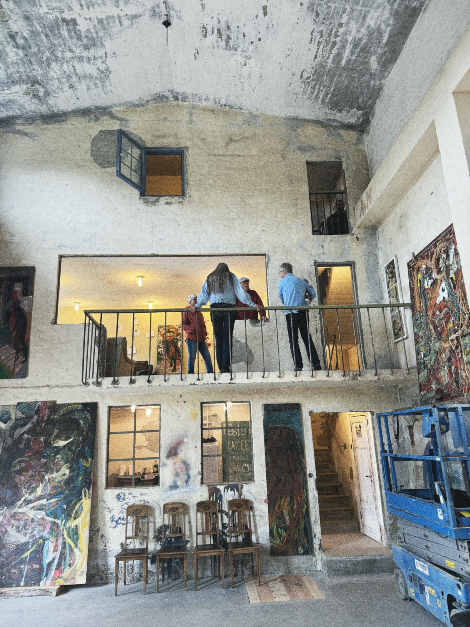 The internal balcony seen from the machine hall below, people leaning on the railing, paintings on the wall underneath.