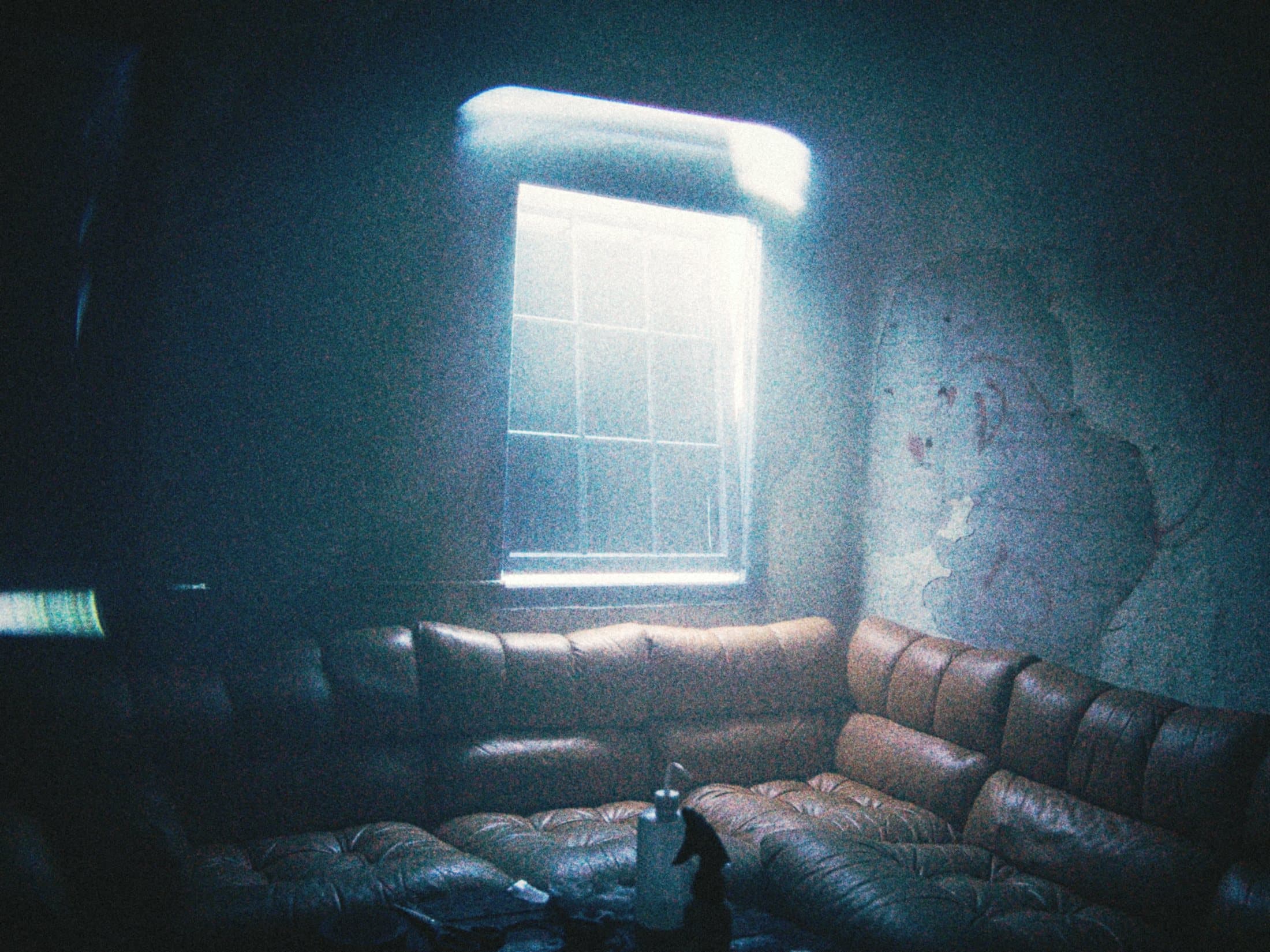 A large leather sofa in a dark room, lit by a single bright window.