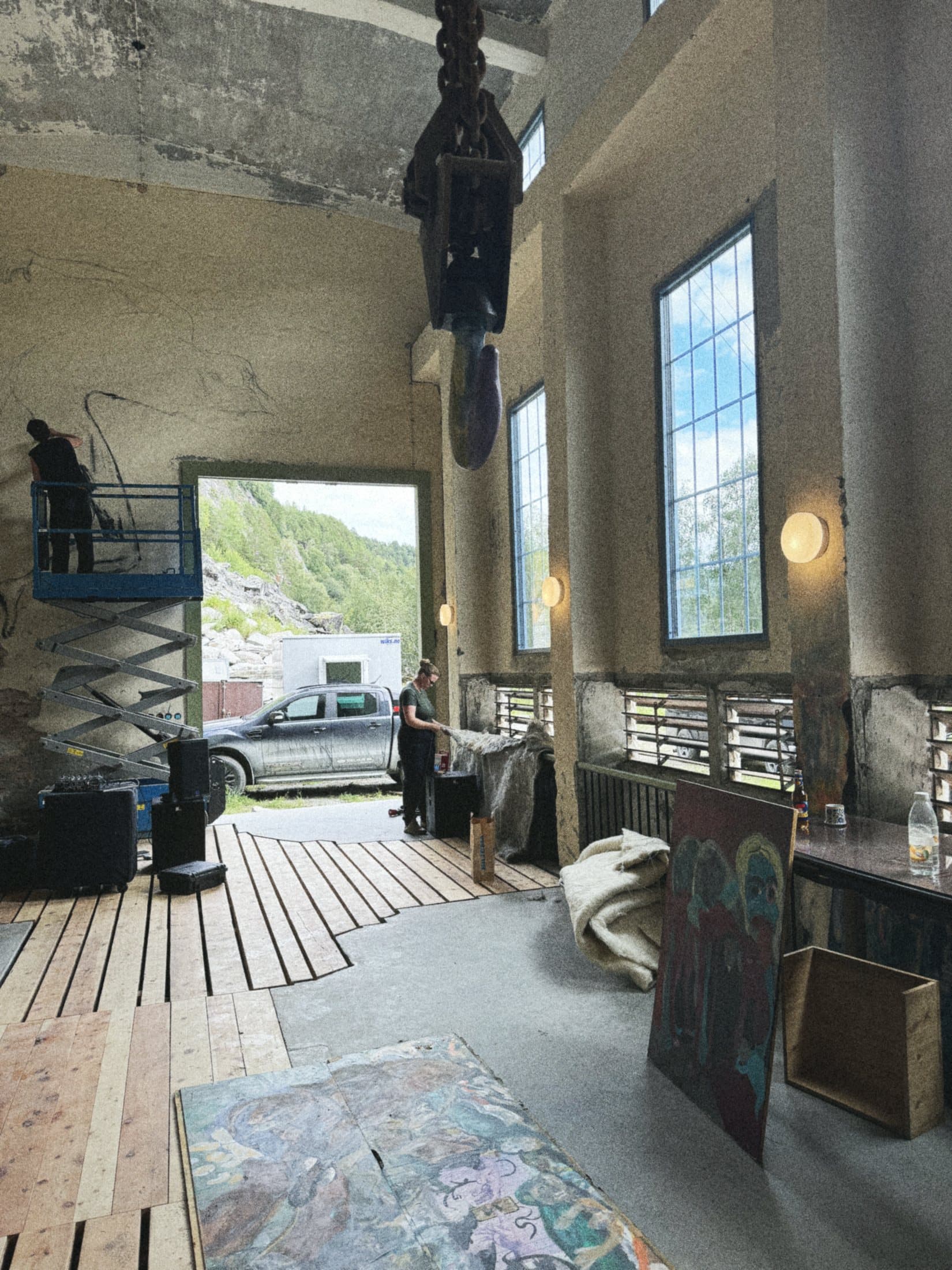 The machine hall in daylight with its big doors open to the valley, a scissor lift and work in progress on the floor.