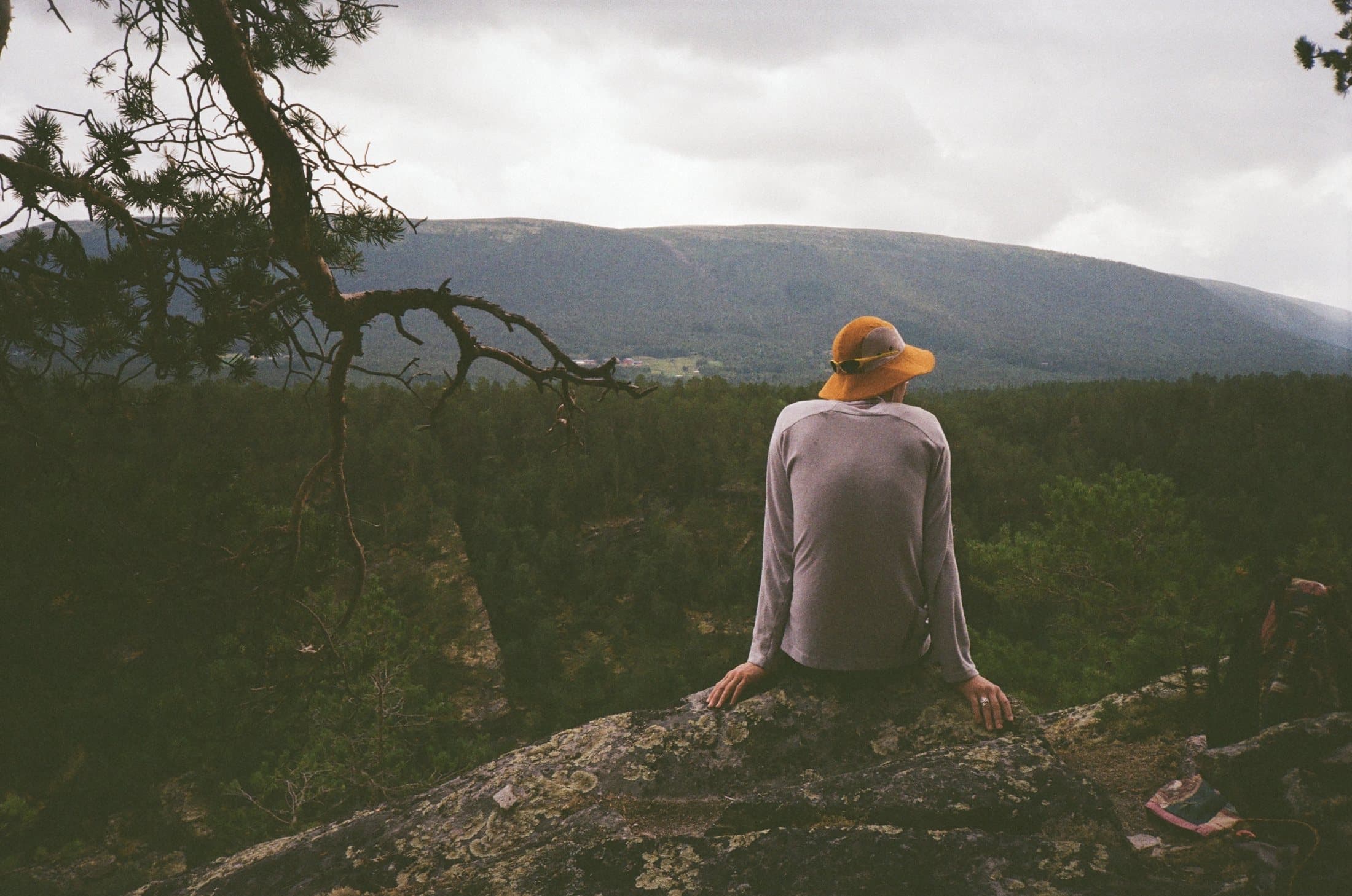 Someone in an orange cap sitting on a rock, looking out over the valley.