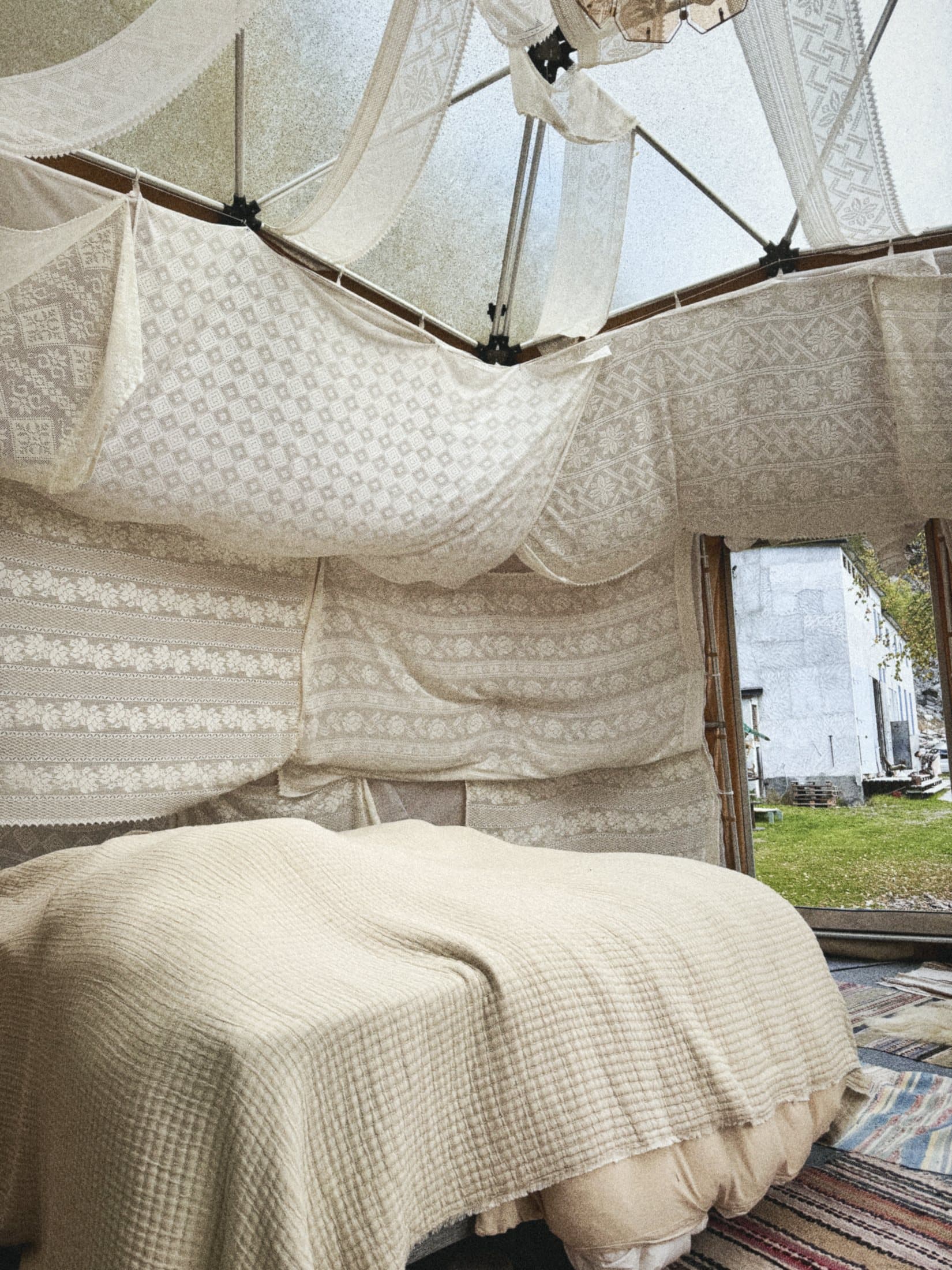 A bed inside a geodesic dome draped with white lace, the trees visible through the panels.