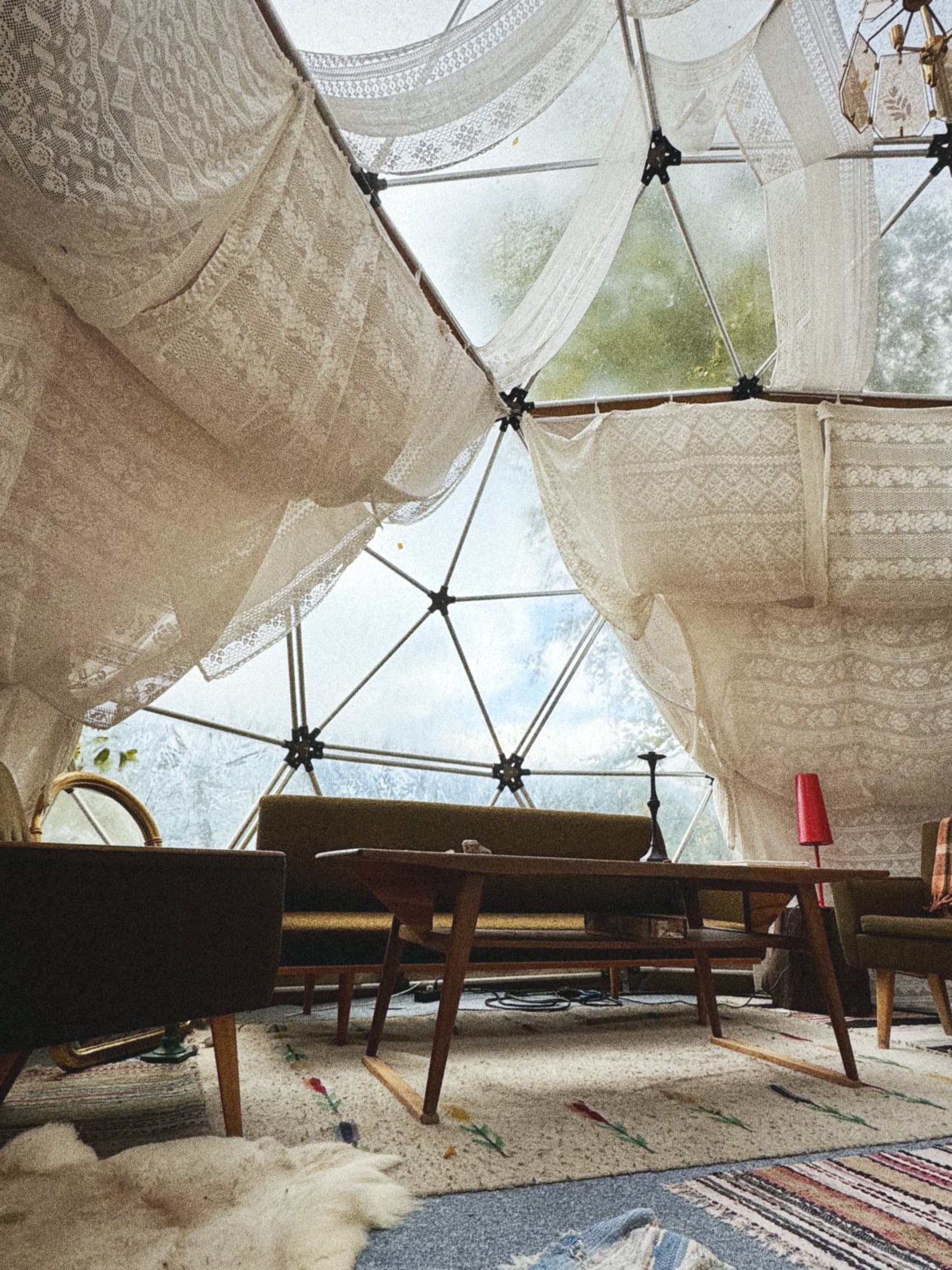 Inside a dome with a sofa, a table and rugs, lace curtains drawn back from the clear panels.