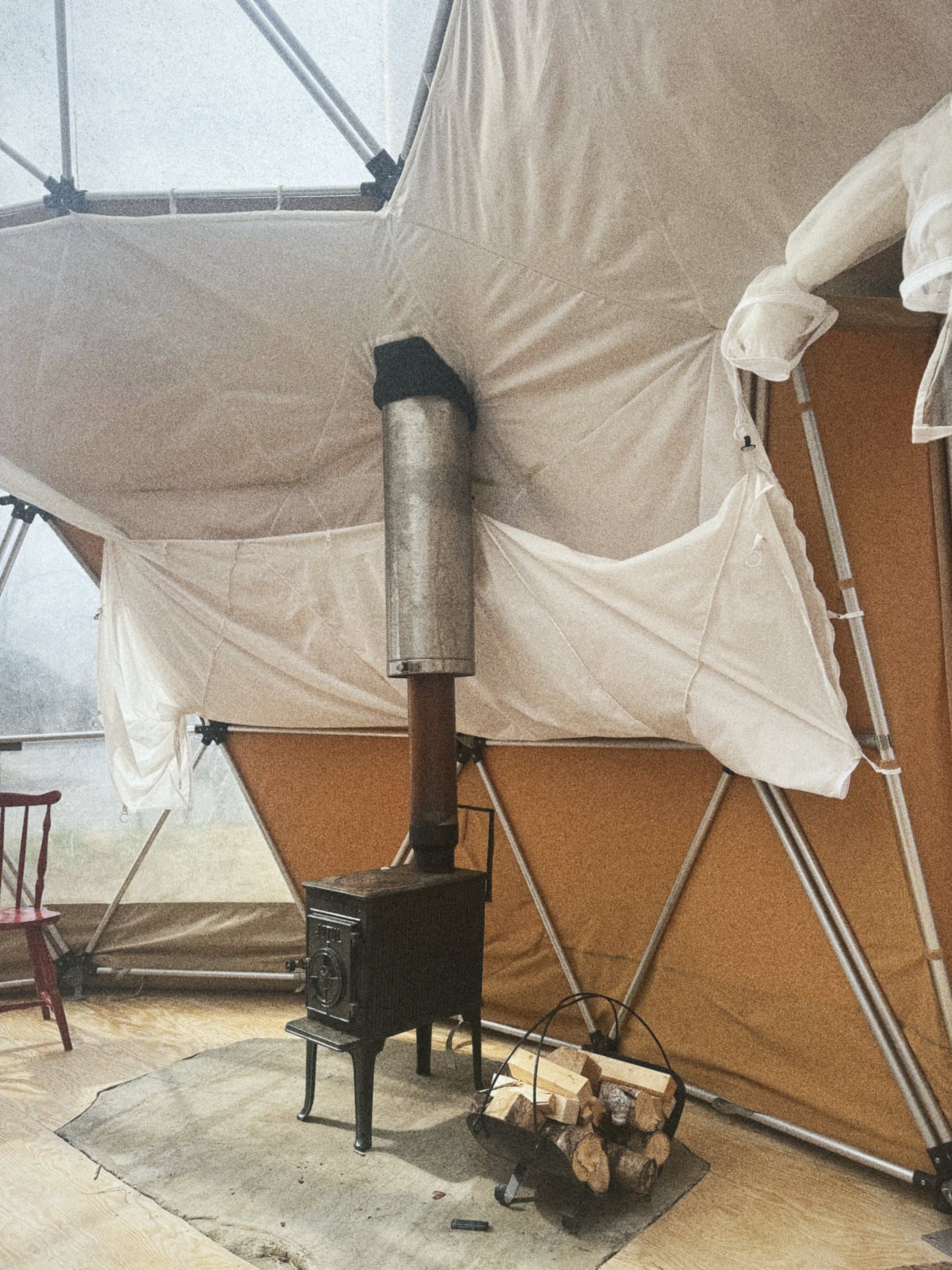 A small black wood stove with firewood beside it inside a canvas dome.